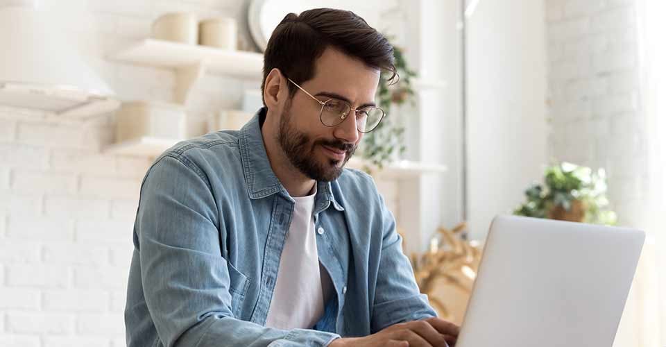 Focused young man wearing glasses using laptop to learn about home purchase in Florida