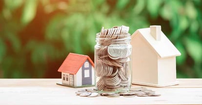 Glass jar full of coins and house model for real estate investment