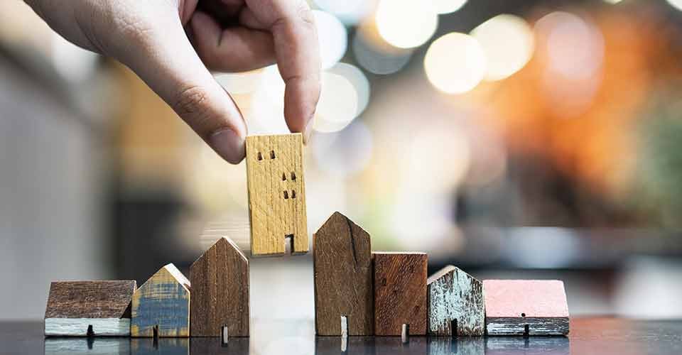 Hand choosing mini wood house model for real estate investment