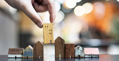 Hand choosing mini wood house model for real estate investment