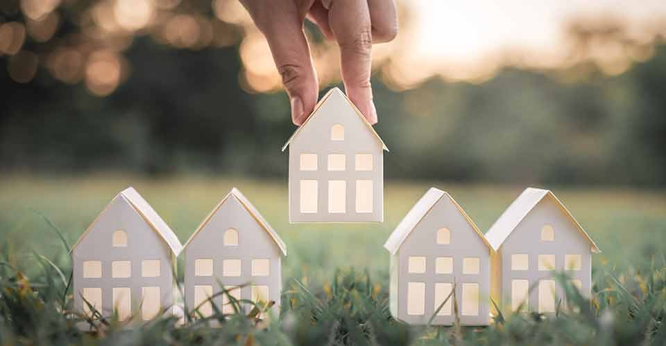 Hand choosing white paper house model from group of house