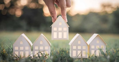 Hand choosing white paper house model from group of house