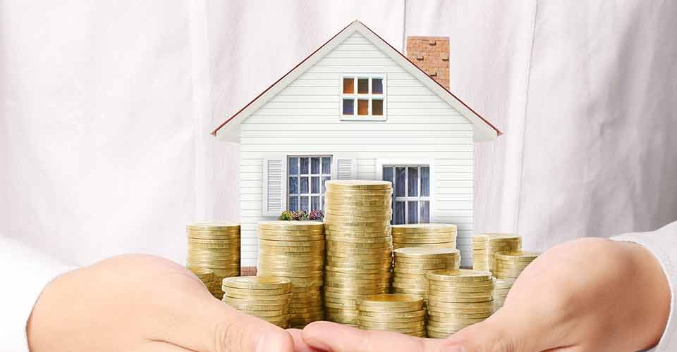 Hand holding a model house and stack of coins