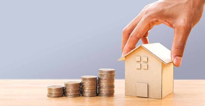 Hand holding house model and money stack on wooden table