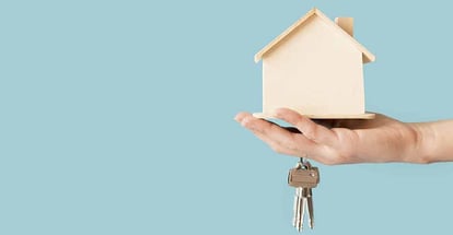 Hand holding keys and wooden house model