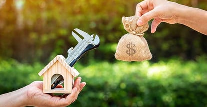 Hand holding wooden home with repairing tools and money bag