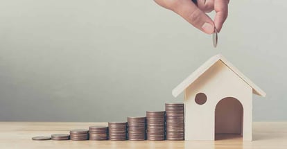 Hand putting money on coin stack with wooden house