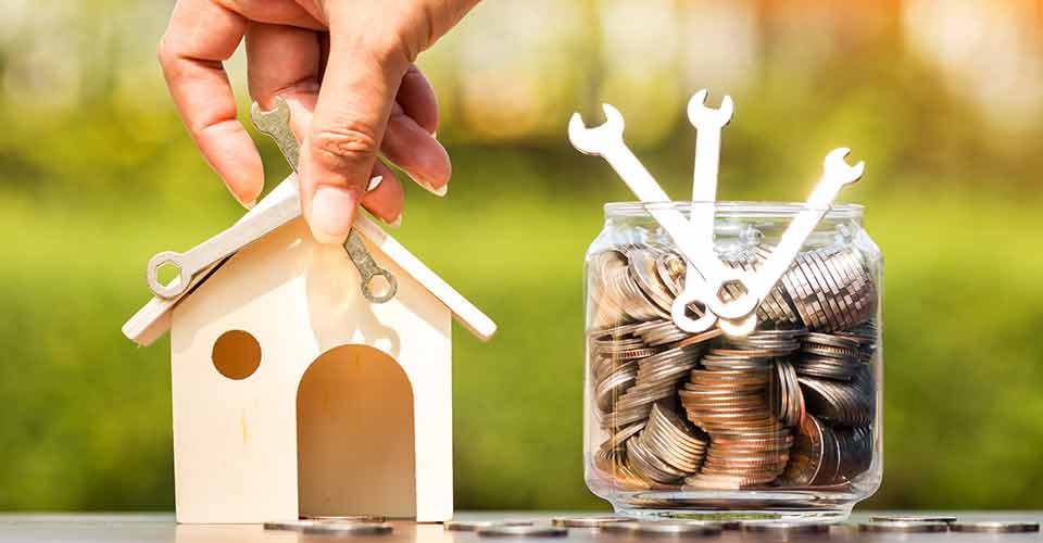 Hand repairing wooden house and bottle bank with money