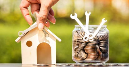 Hand repairing wooden house and bottle bank with money