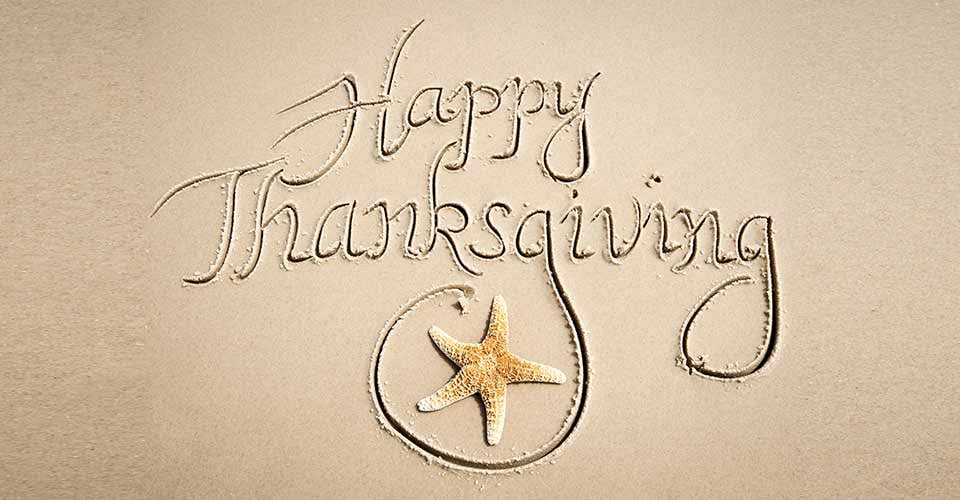 Happy Thanksgiving message handwritten in calligraphic script on smooth sand beach