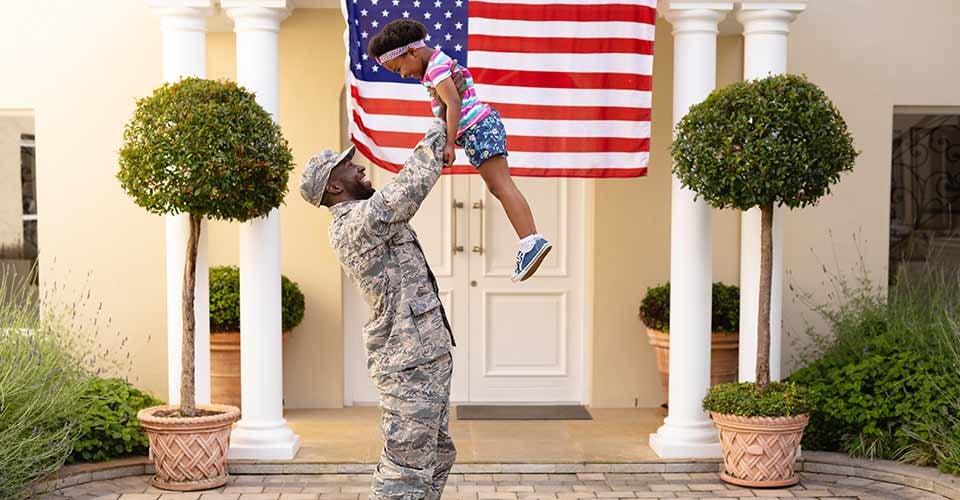 Happy african american military father holding daughter in front of their new house