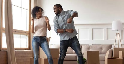 Happy African couple dancing with boxes together in new house on moving day