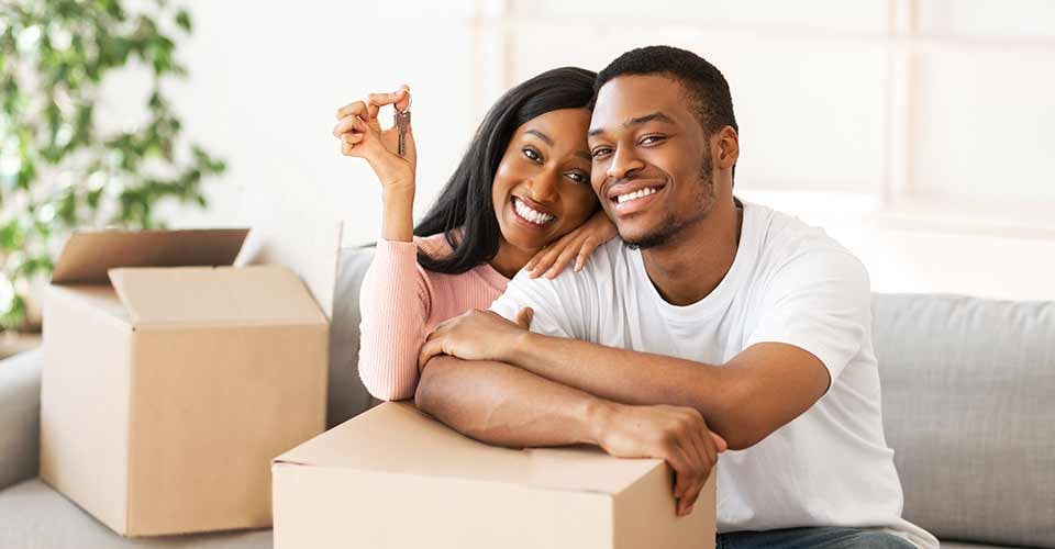 Happy black couple with house key and carton boxes smiling