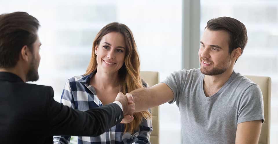 Happy couple handshaking realtor after house purchase