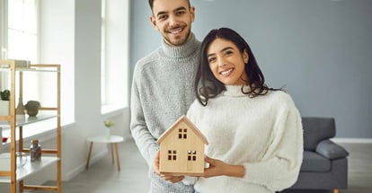 Happy couple holding a house model in their hands while standing in a room at home