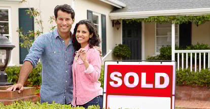 Happy couple outside their new home with sold sign