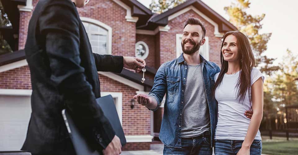 Happy couple taking keys of their new house from broker