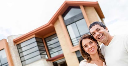 Happy couple with their new house at the background and smiling