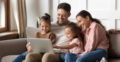 Happy family with two little daughters using laptop together and sitting on sofa at home