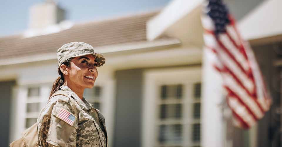 Happy female soldier looking away with a smile while standing outside her house