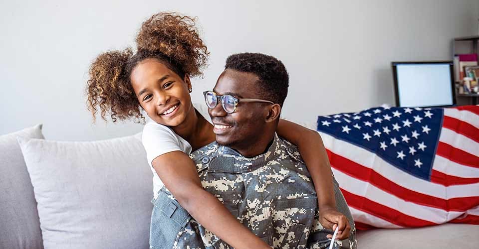 Happy little girl hugging father in military uniform at new home