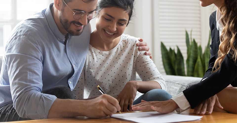 Happy married couple signing contract at meeting with realtor