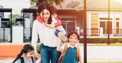 Happy mother walking out from home holding hands with her kids going to school