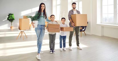 Happy smiling family in new home holding unpacked cardboard boxes