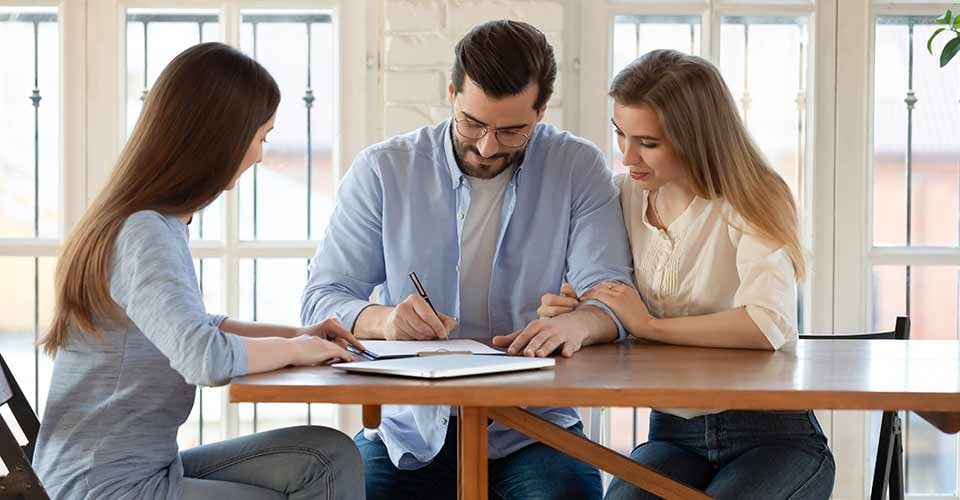 Happy young couple signing house purchase contract with professional realtor