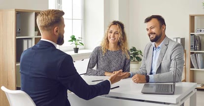 Happy young couple sitting at table listening to realtor