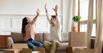 Happy young couple sitting on couch and celebrating moving day in new house