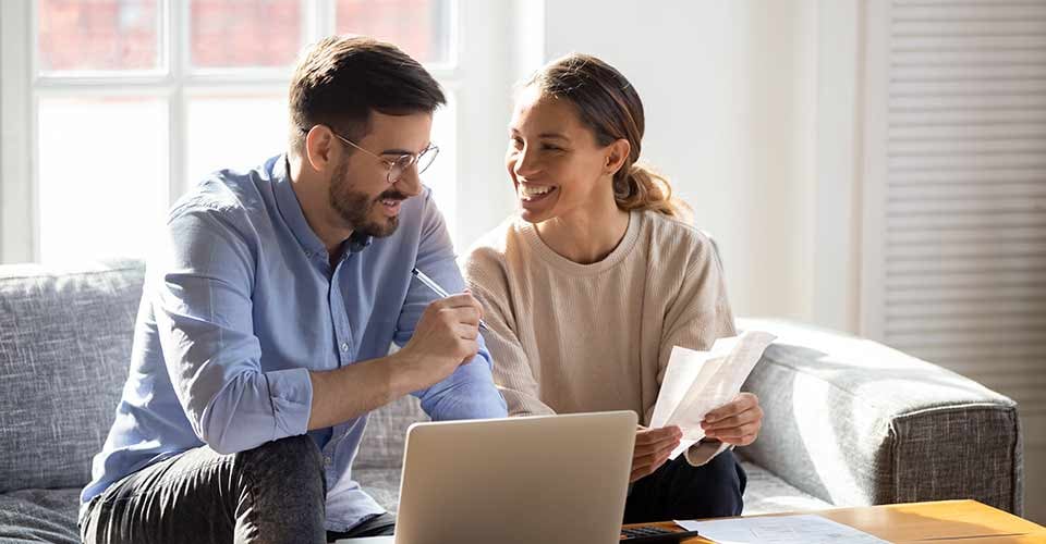 Happy young married couple sit on couch and look at mortgage document