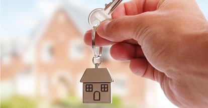 Holding keys on house shaped keychain in front of a new home
