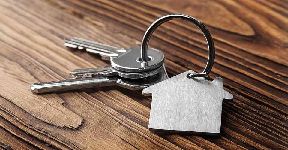 House key on house shaped keychain on wooden floorboard