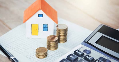 House model and coin stack with calculator on table