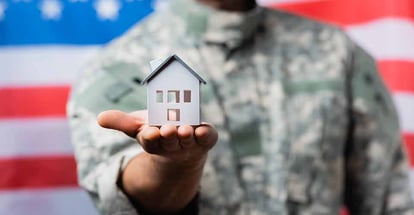 House model in hand of military man in uniform near american flag