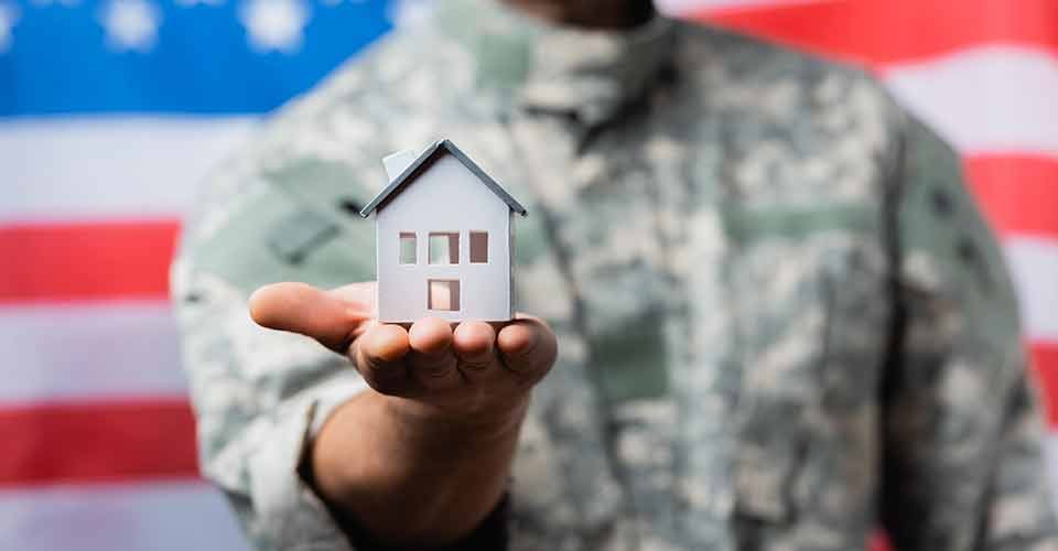 House model in hand of military man in uniform near american flag