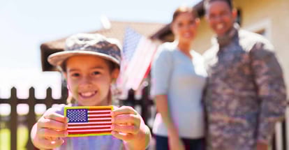 Little girl holding american flag badge in front of military parents outside new home