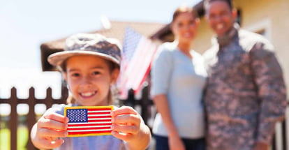 Little girl holding american flag badge in front of military parents outside new home