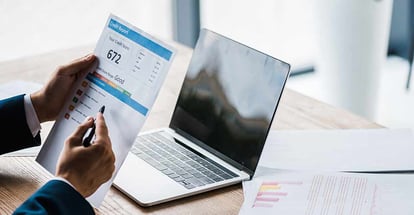Man holding paper with credit report letters near laptop