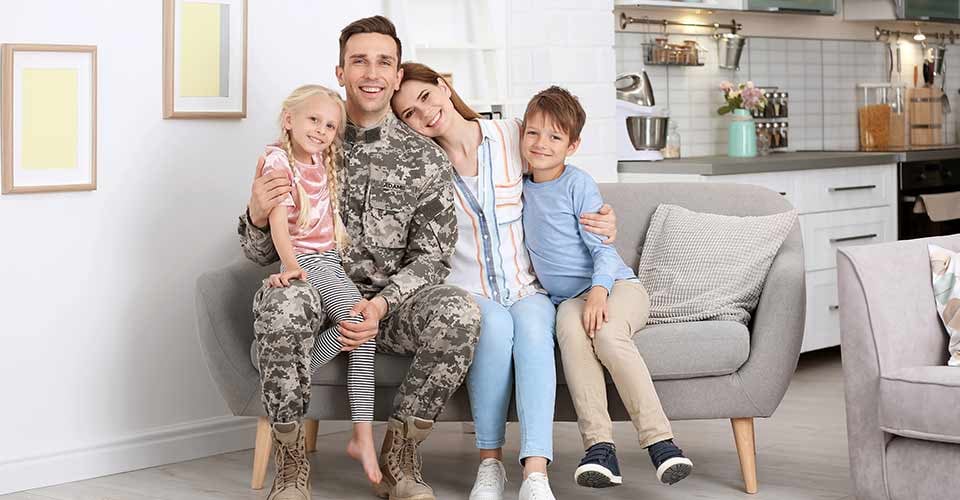 Man in military uniform with his family on sofa at new home