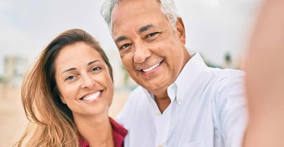 Middle age hispanic couple smiling and taking selfie at the beach