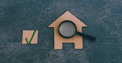 Miniature cardboard house with magnifying glass analyzing it