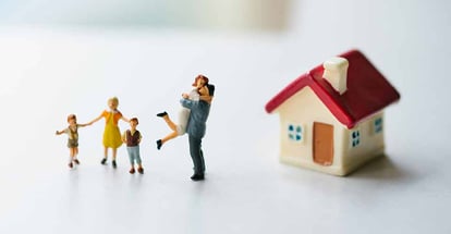 Miniature happy family standing outside mini house