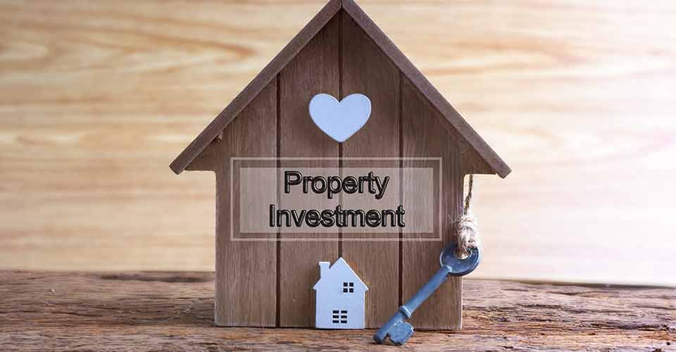 Miniature home made from wood and word property investment written on wooden base