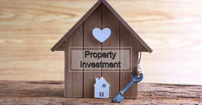 Miniature home made from wood and word property investment written on wooden base