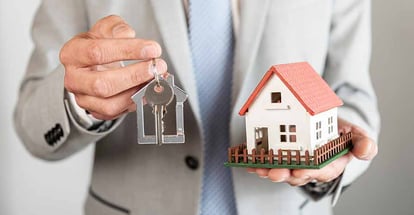 Model house and keys being held in hands by a person
