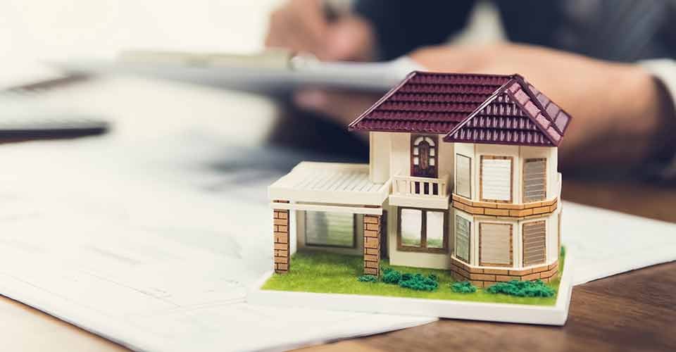 Model house on a desk and a buyer signing documents