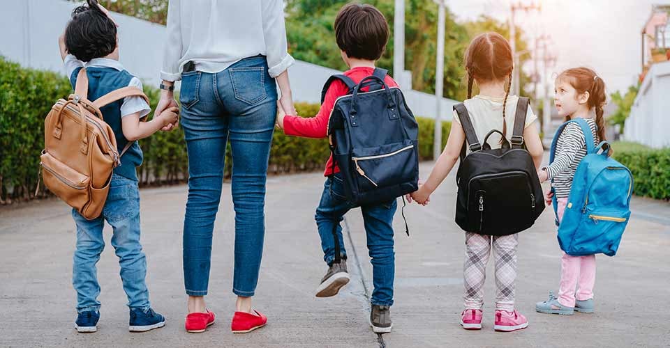 Mother and pupil and kids holding hands going to school