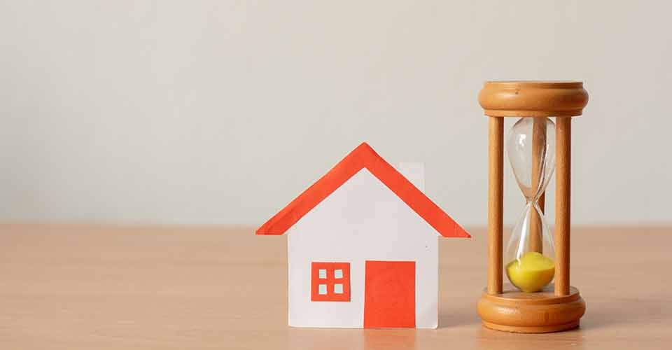 Paper house with hourglass on wood table